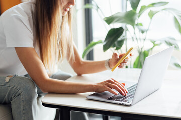 Young woman holding credit card and using laptop computer. Online shopping, e-commerce, internet banking, spending money, working from home concept