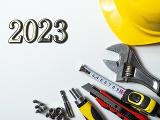 2023 with construction tools, yellow hard hat on white background with copy space. New Year and Christmas construction greeting card. For advertising or web design. Repair home at Christmas. Flat lay.