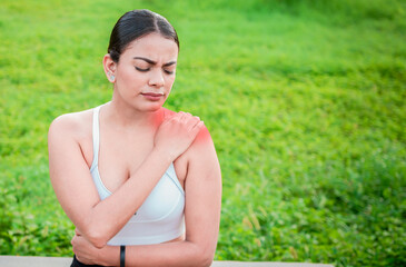 Young woman with shoulder pain sitting outside. Girl suffering from shoulder pain sitting outdoors. Woman sitting and stressed with shoulder pain outdoors. Girl with shoulder pain outdoors