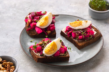Open sandwiches on rye bread with beetroot salad, boiled egg and microgreens on a ceramic plate on a gray concrete background. Swedish cuisine.