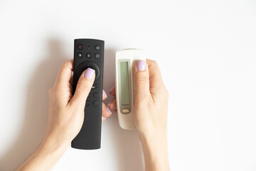 Two remote controls in female hands on a white background close-up, TV