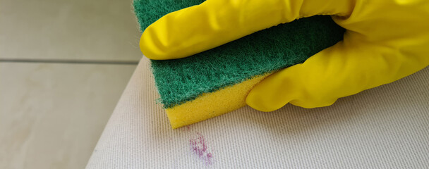 Gloved hand cleans stain with light white cloth on furniture with washcloth