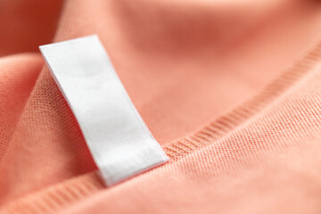 Blank white laundry care clothes label on pink fabric texture background