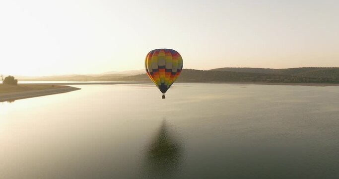 Hot air balloon passing low above a lake with sunrise reflections