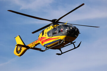 Żółty helikopter na niebieskim niebie w powietrzu.  - obrazy, fototapety, plakaty