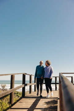 Romantic Senior Couple Taking A Walk On A Boardwalk At The Beach