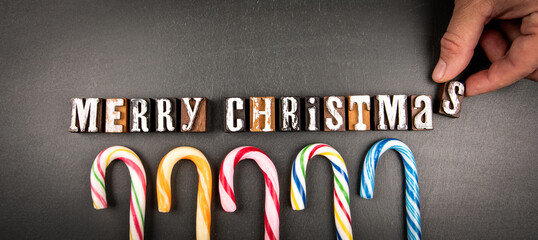 Merry Christmas. Wooden alphabet letters and candy canes on a dark chalkboard background
