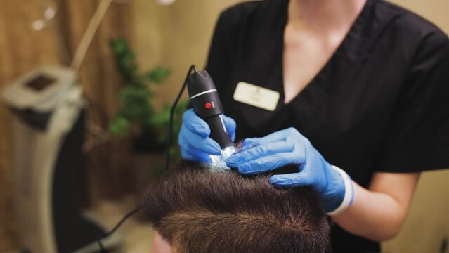 a doctor examines head skin and hair of a patient with suspected alopecia. close up view of hands with trihoscope on head of pacient.