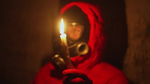 Ukraine war. A man in a gas mask hides in a bomb shelter from rocket fire; there is no electricity, he lights a candle