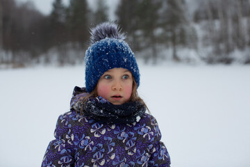 A girl in winter on the street with rosy cheeks and a surprised expression on her face