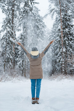 Happy woman walking in winter forest during heavy snowfall, watching falling snowflakes in park