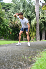Active fit Asian man in sportswear sweating and exhausted after a long run in the park.