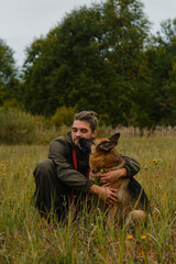 Naklejka na ściany i meble Concept of love and loyalty with animal. Male pet owner sits in grass in autumn and hugs dog. Young Caucasian man with dreadlocks and beard, German shepherd licks his face.