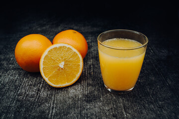 Freshly squeezed orange juice in a glass with freshly sliced ​​orange with a dark background.