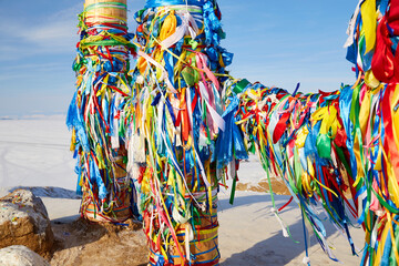 Multicolored ribbons on wooden ritual pillars at Cape Burkhan. Lake Baikal in winter, Olkhon Island.