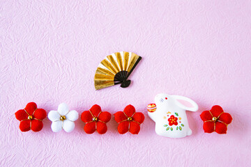 日本の正月イメージ　干支の卯の人形と紅白のちり緬の梅と扇のデザイン（ピンクの和紙の背景）