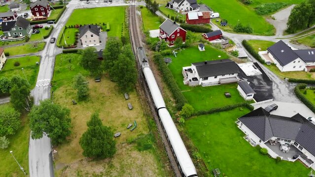 Aerial: Fl&aring;m train going through a valley among green meadows and some houses