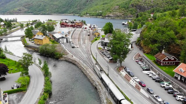Aerial: train by a river entering Fl&aring;m station