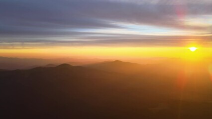 Aerial view of dark mountain hills with bright sunrays of setting sun at sunset. Hazy peaks and misty valleys in evening