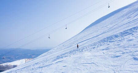 Hiker walking down the ski slope covered with snow under the cable lift in the winter