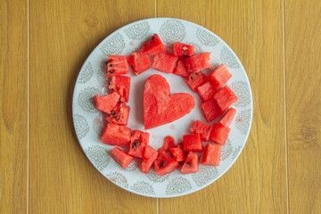 Heart-shaped watermelon surrounded by pieces on a plate on a wooden table