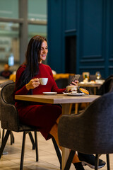 Shot pregnant woman sitting in a restaurant using her phone and drinking coffee. Woman scrolling on her phone, having a break from work