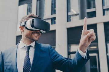Smiling bearded businessman with stubble wearing VR glasses, viewing something in virtual reality