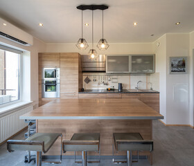 Modern interior of wooden kitchen in luxury apartment. Private house. Table, chairs, counter with sink, home appliances.