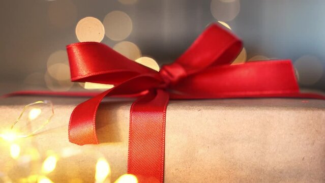 Cozy Christmas gift craft paper box with red ribbon bow. New year eve holiday composition with present handmade box. Christmas eve preparation. Family time, cozy homeю Soft focus