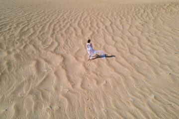 Girl in white dress walking in the sand desert
