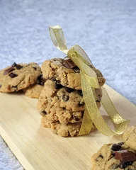 Tuinposter Chocolate chips cookies wrapped on golden ribbon on the wooden board with the blurry background © Girygen/Wirestock Creators