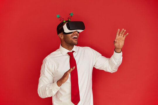 Focused Man Trying VR. Portrait of Amazed Multiracial Guy Discovering New Technologies Wearing Virtual Reality Headset, Futuristic 3d Vision. Indoor Studio Shot Isolated on Red Background 