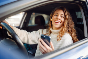 Portrait of a young woman texting on her smartphone while driving a car. Car sharing, rental service or taxi app.