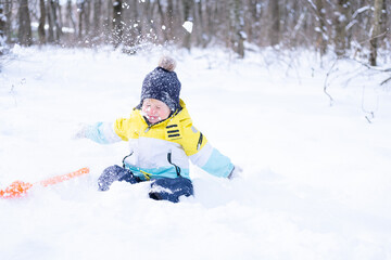 Fototapeta na wymiar Cute smiling little boy with shovel playing with snow outdoors in winter forest