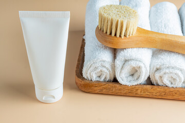 SPA cosmetics, woman body and skincare products on wooden tray on beige background. Natural bristle dry massage brush and body or face cream in white plastic tube.