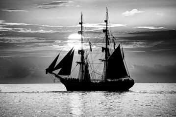 Sailboat sailing in the sea. Sunset background. Black and white.