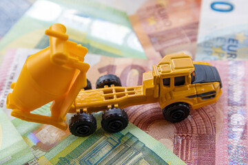 Side view of a toy concrete mixer on the background of different euro banknotes. The concept of...
