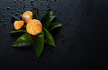 Peeled tangerine with fresh leaves and dew drops on a black background. Place for text