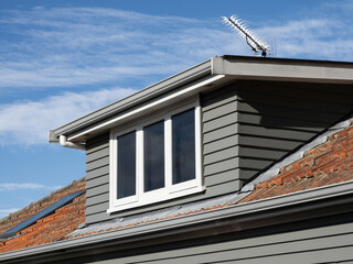 View of gray shed roof dormer loft with white window and clay colored tiles