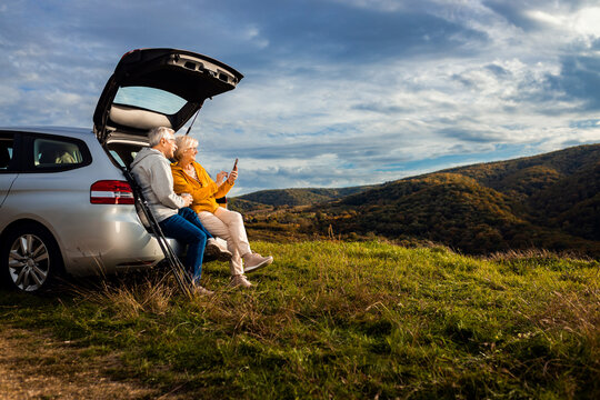 Senior couple sitting against the car, resting after hiking in countryside.