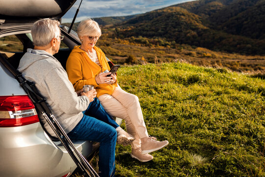 Senior couple sitting against the car, resting after hiking in countryside.