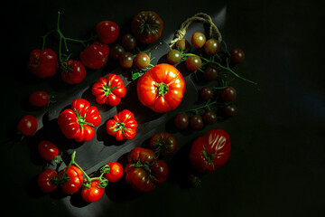 Kitchen still life, top view - tomatoes of different sizes, varieties and shades. the photo is made in a dark key, the chiaroscuro pattern emphasizes the style. product advertising. copy space