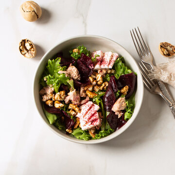 bowl with salad with tuna, beets, cheese and nuts on a light table
