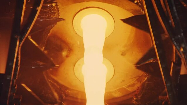 Slow motion of Molten glass pouring out of a Glass melting furnace in a bottle production facility.