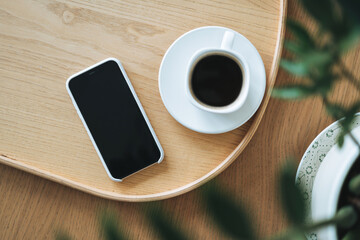 Fototapeta na wymiar Top view of smartphone screen and cup of coffee through green houseplant