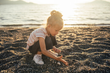 Cute little girl playing on the beach at sunset.