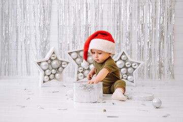 Merry Christmas and Happy Holidays. Cute little baby in a Christmas decorated house. The kid enjoyed the holiday. Portrait of a baby with a gift on a light background.