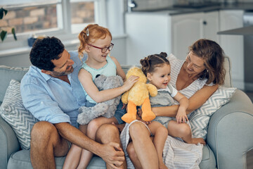 Family, happiness and love on home sofa with children holding stuffed animal toys while bonding with mom and dad parents. Woman, man and girl kids together for care, development and quality time