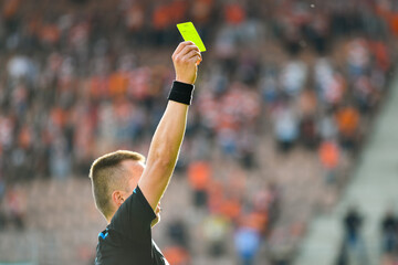 Referee shows yellow card during soccer match at the stadium.