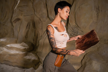 sexy archaeologist in tank top looking at ancient map near rock in desert.